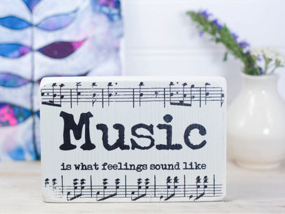 Small wood sign in whitewash with music notes and the saying "Music is what feelings sound like".