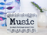 Small wood sign in whitewash with music notes and the saying "Music is what feelings sound like".